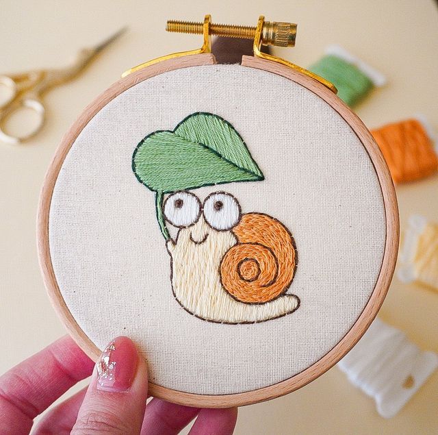 a person holding up a small embroidery hoop with a snail on it's face