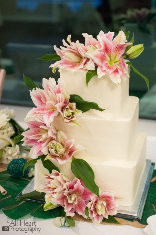 a wedding cake with pink flowers and greenery on the top is ready to be cut