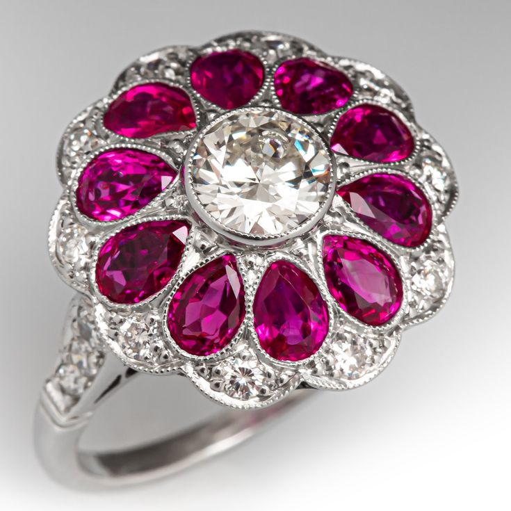 This spectacular ring is centered with one (1) bezel set round brilliant cut diamond. The center diamond is bordered with ten (10) bezel set pear cut natural rubies, and ten (10) bead set round brilliant cut diamonds. The shoulders of the ring are each accented with three (3) bead set round brilliant or old European cut diamonds. The gemstones are bordered with milgrain edging. The under gallery features a pierced design with ornate scroll motifs. The ring measures 17.8mm at the top, rises 8.3mm Mafia Princess, Antique Cocktail Ring, Diamond Ring Platinum, Antique Engagement Rings Sapphire, Estate Jewelry Rings, Wedding Ring Diamond Band, Marquise Diamond Ring, Three Stone Diamond Ring, Princess Jewelry