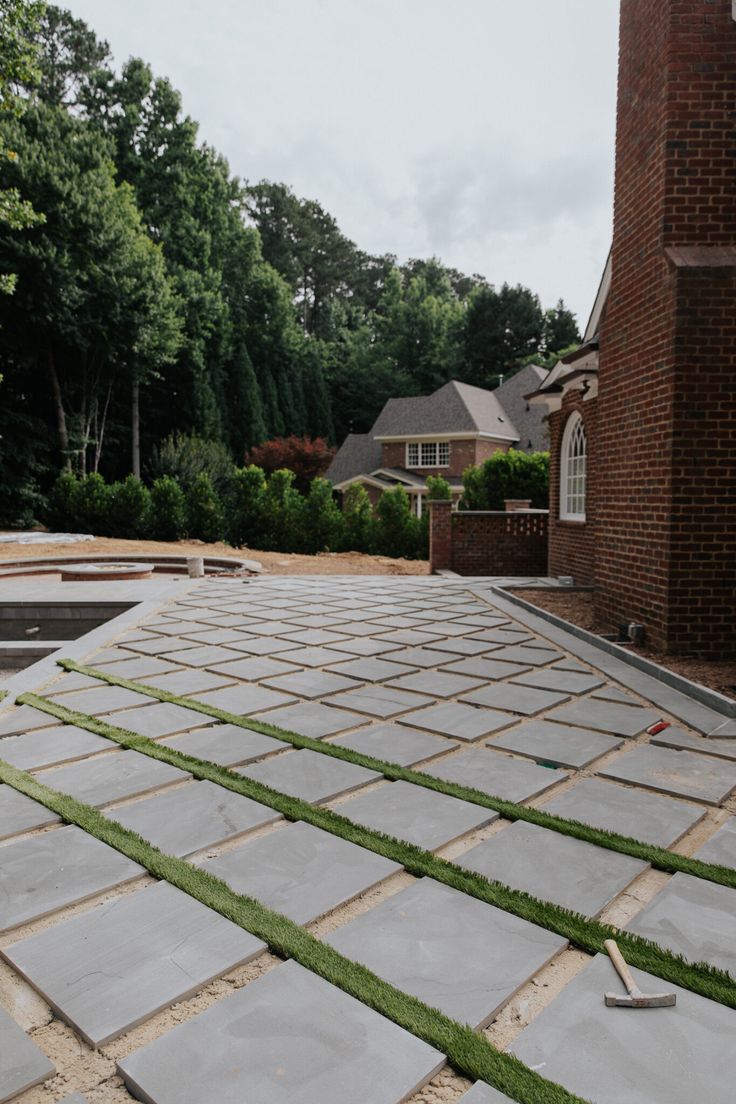 an outdoor patio being built with grass growing on the ground and brick building in the background