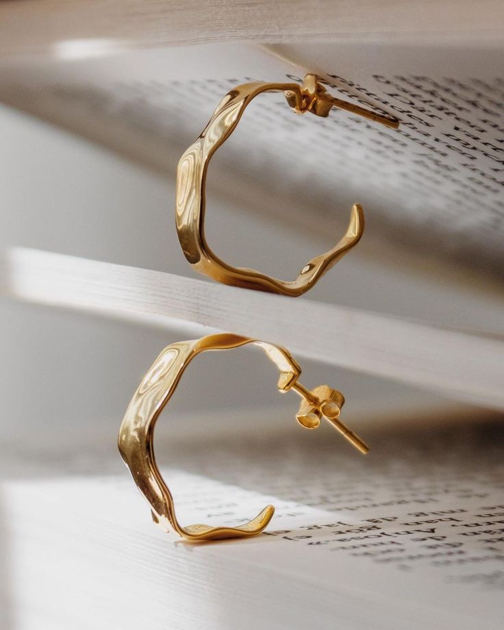 two pairs of gold - plated metal hoop earrings on top of an open book