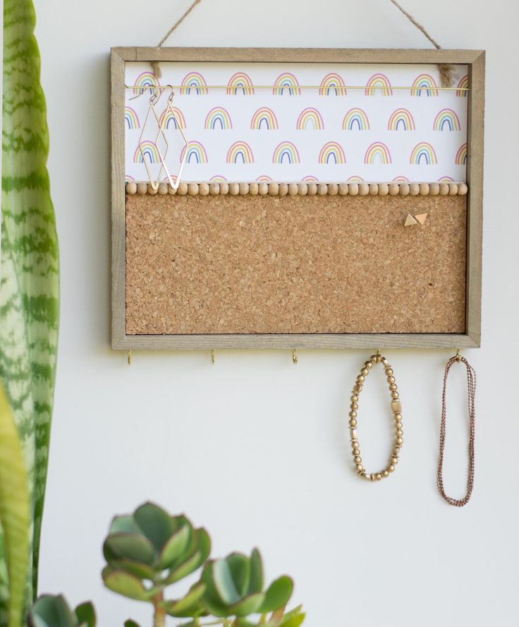 a cork board hanging on a wall next to a potted plant and a necklace