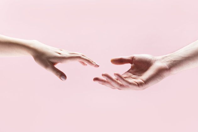 two hands reaching out towards each other against a pink background with only one hand touching the other