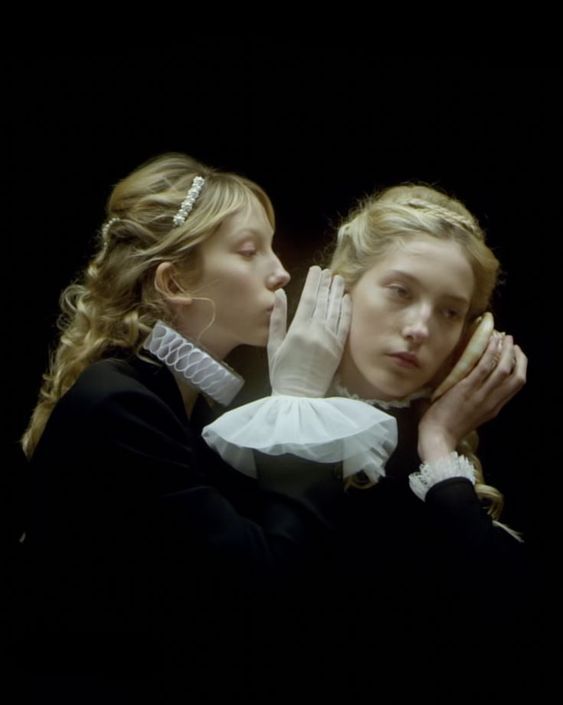 two young women are touching each other's faces in front of a black background