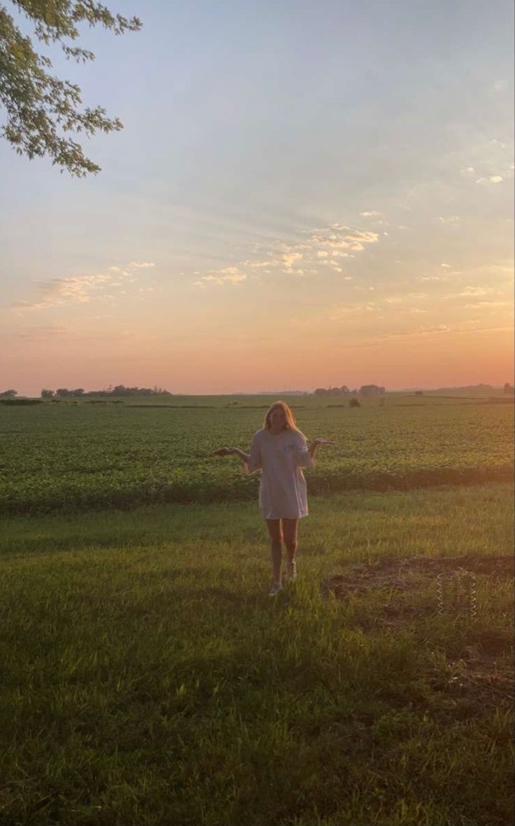 a woman standing in the middle of a field at sunset