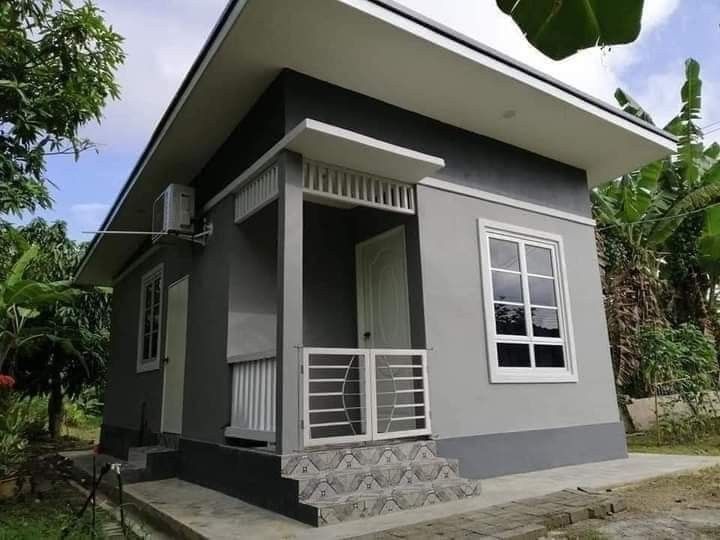 a small gray and white house sitting on top of a lush green field next to trees