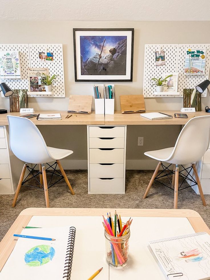 a desk with two white chairs and some pictures on the wall next to each other