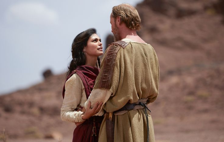 a man standing next to a woman on top of a desert field with mountains in the background