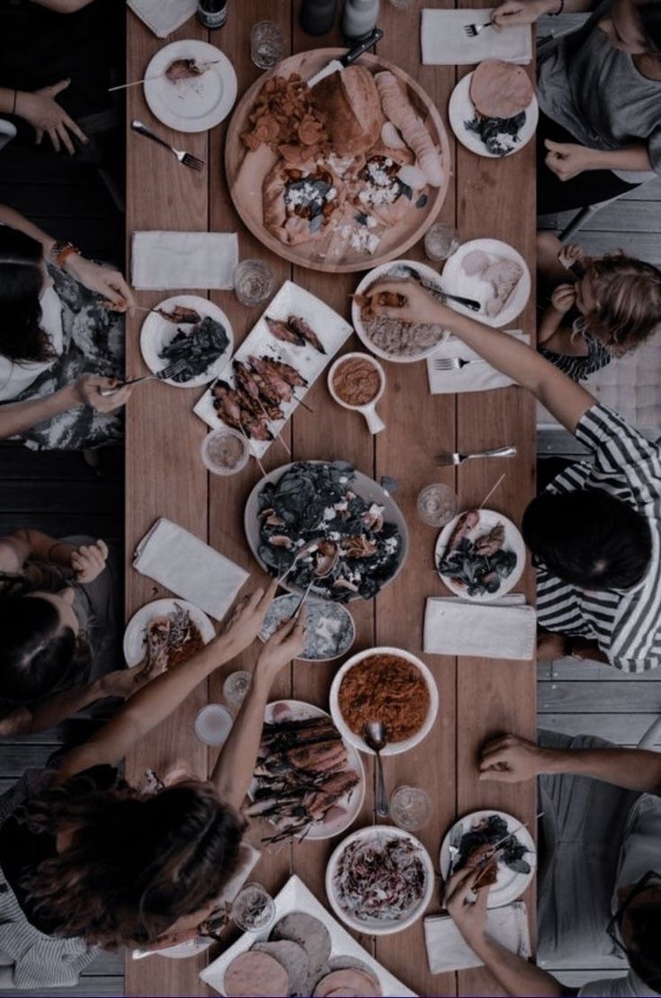 a group of people sitting around a wooden table eating food and drinking wine together, top view from above