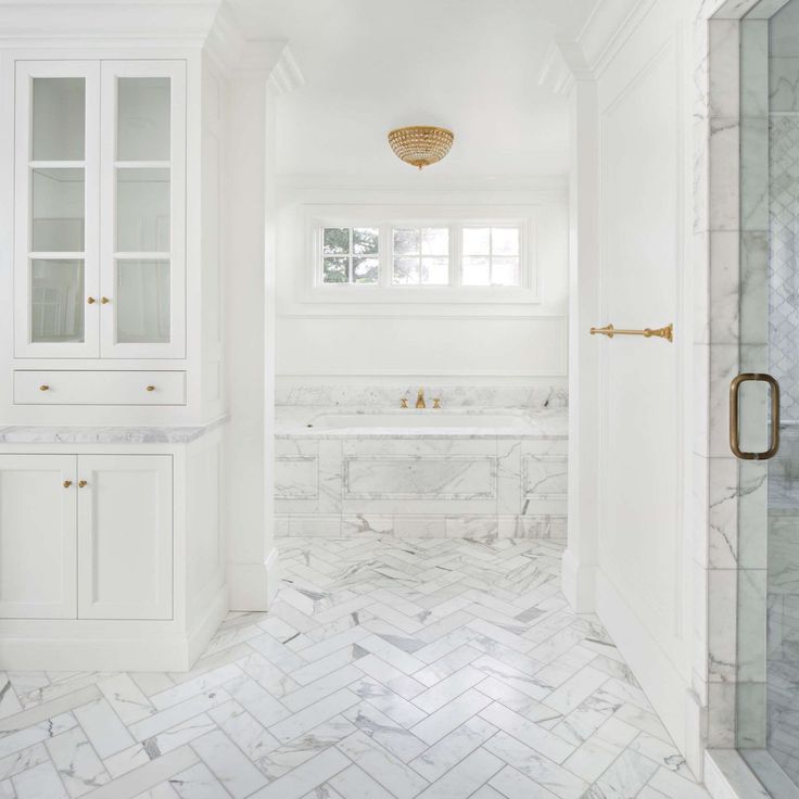 a white bathroom with marble flooring and large glass shower door, built in cabinets