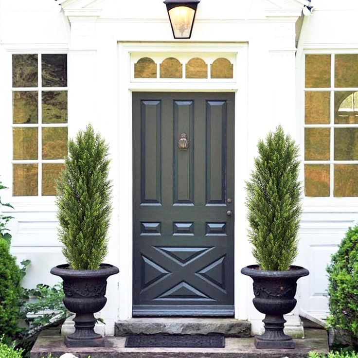 two large planters are in front of the door to a white house with black trim