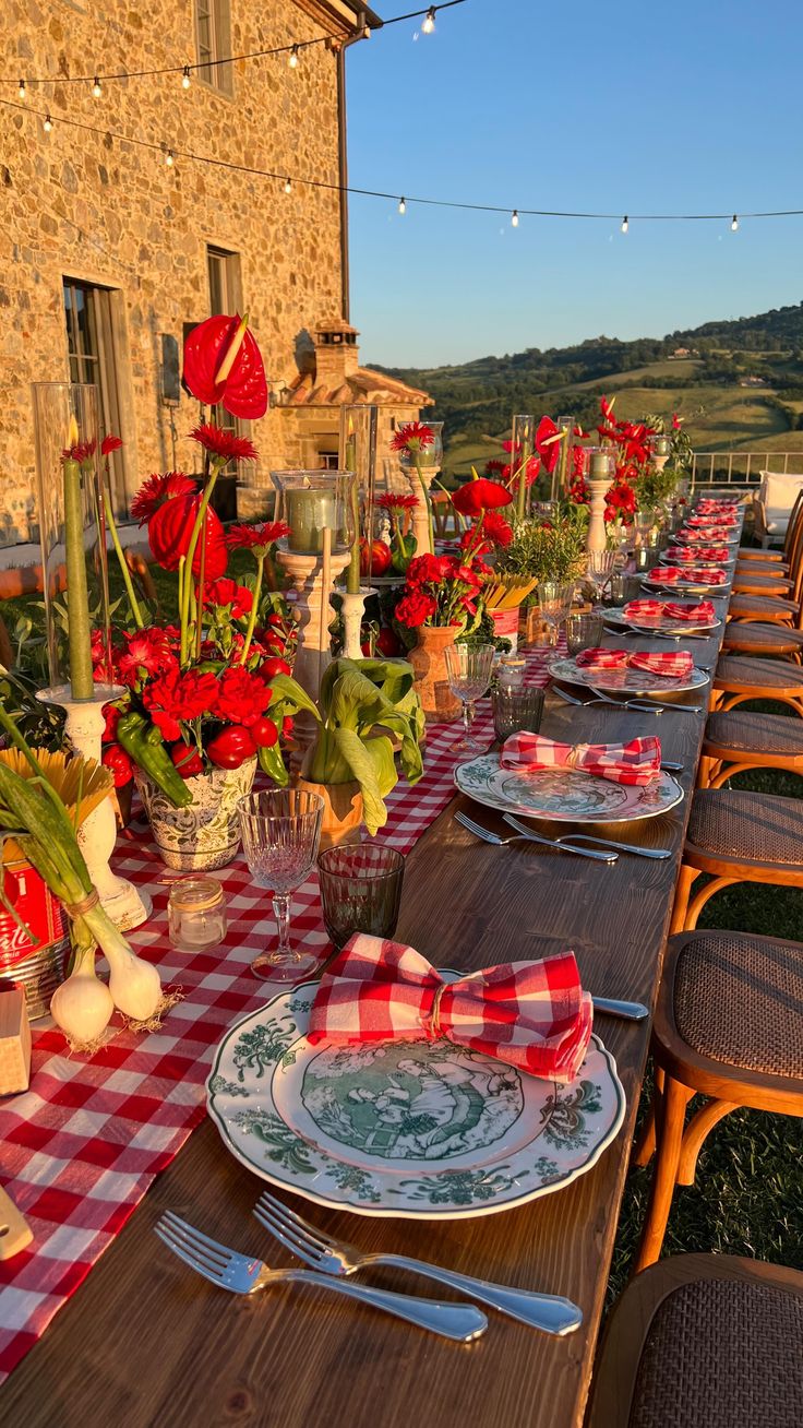 a long table set with place settings and red flowers in vases on the tables