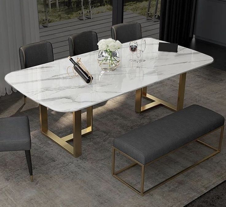 a marble dining table with gold legs and grey upholstered chairs in front of a large window