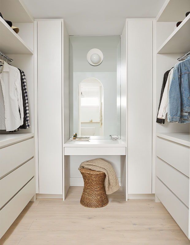 a bathroom with white walls and cabinets, including a stool in front of the mirror