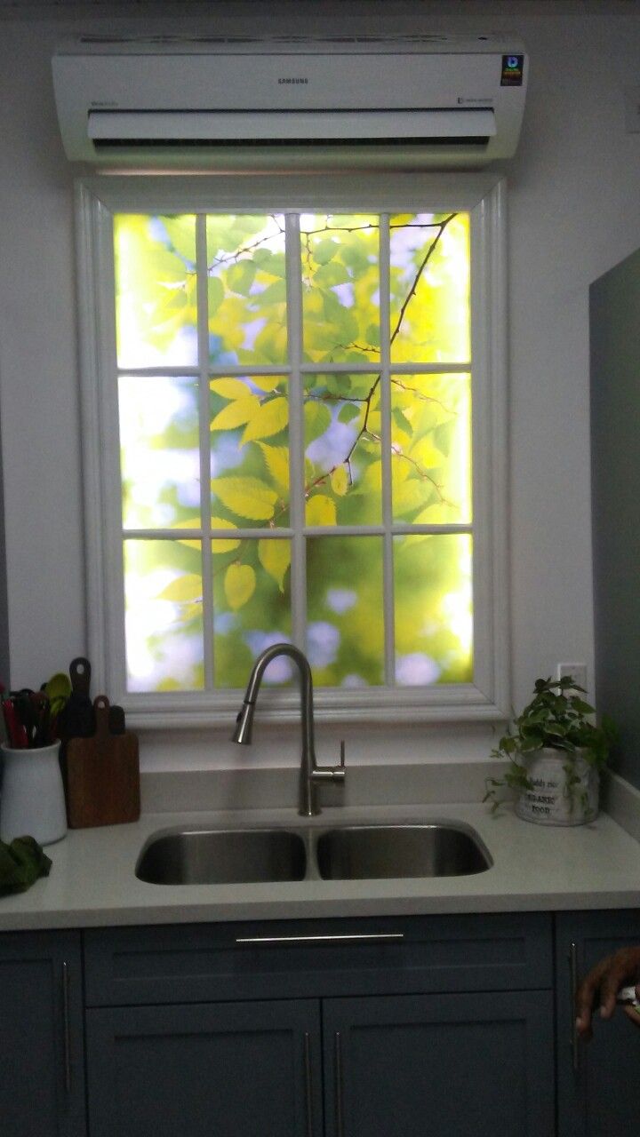 a kitchen sink under a window in front of a counter with plants and utensils