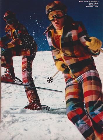 two people on skis in the snow, one wearing goggles and plaid pants