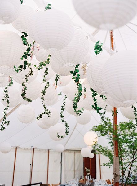 white paper lanterns hanging from the ceiling in a tent with tables and chairs under them