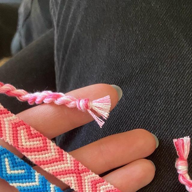 a person holding two different colored bracelets with tassels on each end and one bead in the middle