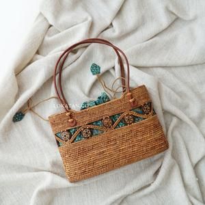 a straw bag with blue and green details on it sitting on a white cloth covered bed