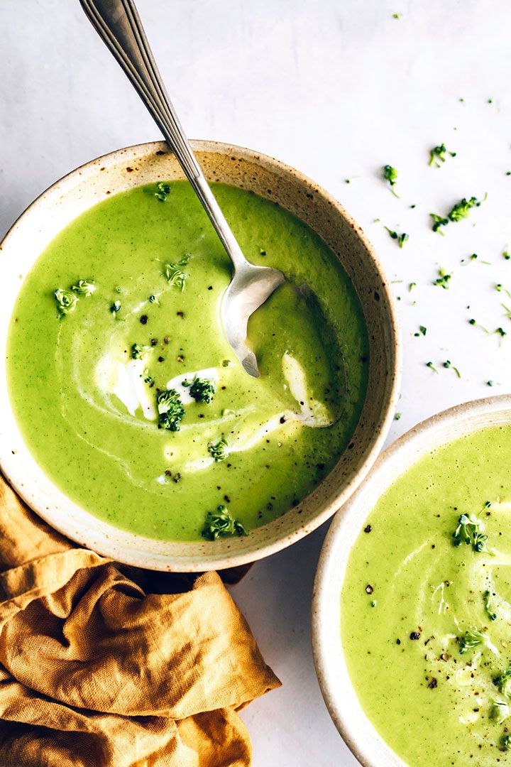 two bowls filled with green soup next to tortilla chips on a white surface