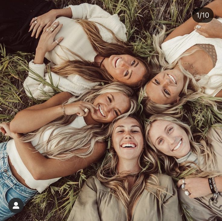 four beautiful women laying in the grass with their arms around each other and smiling at the camera