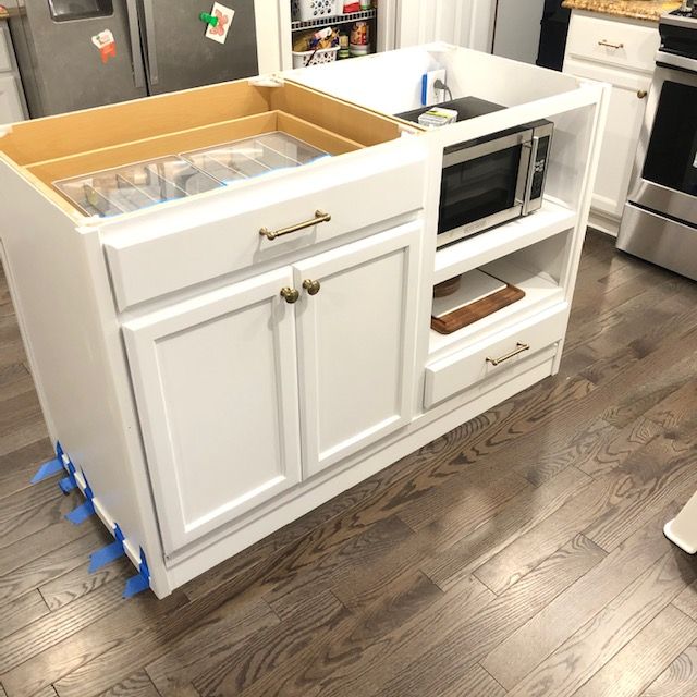 an open cabinet in the middle of a kitchen with white cabinets and wood flooring