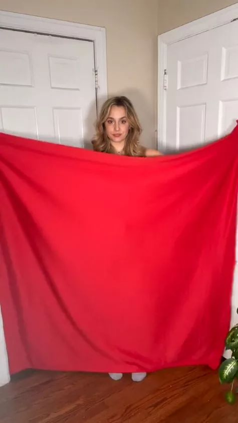 a woman holding up a red cloth in front of two white doors and a potted plant