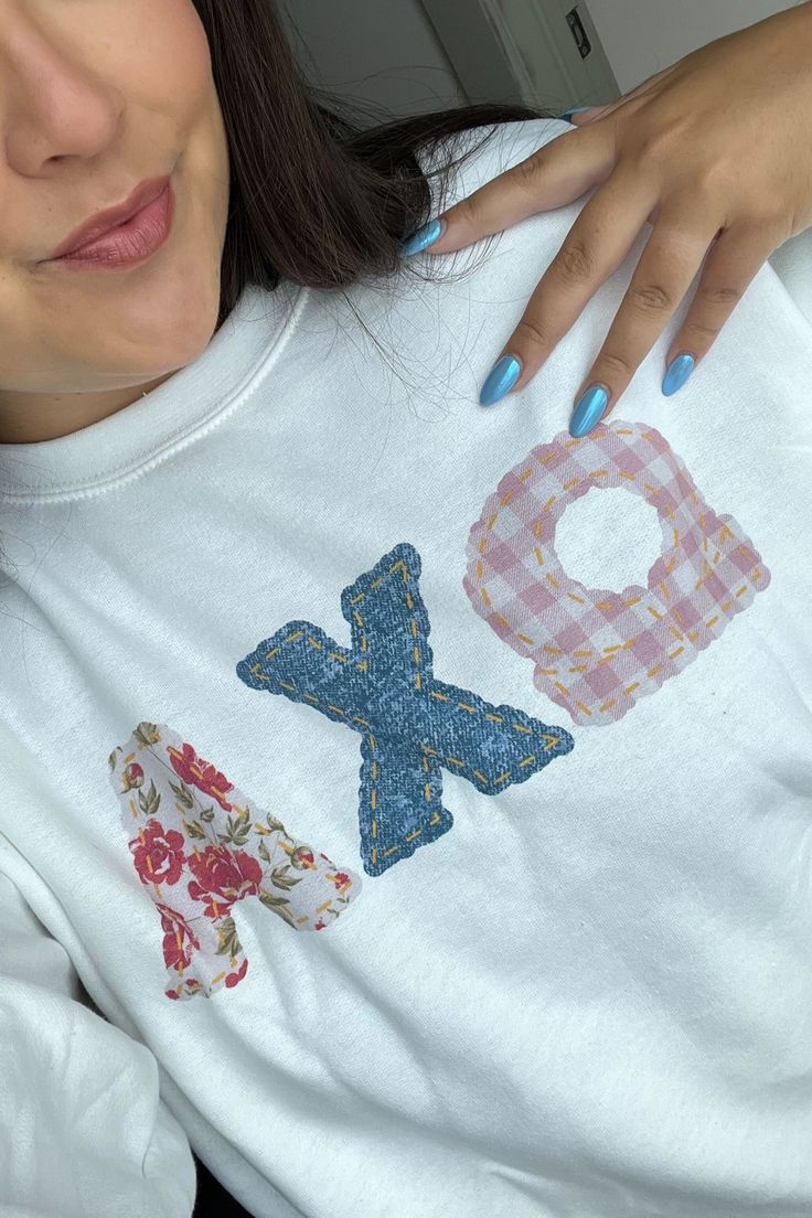 a woman with blue nails is wearing a white shirt that has the letter q on it