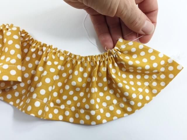 someone is sewing on a yellow and white polka doted skirt with a thread in it