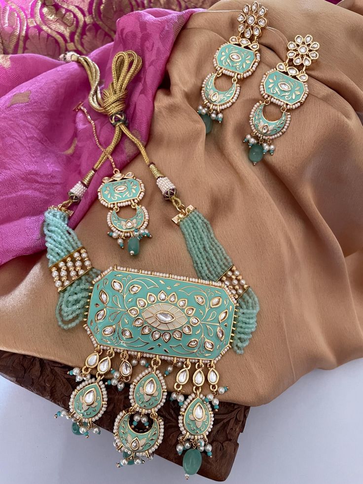 Gorgeous Mintgreen Kundan Choker Set that is trending and a bestseller with us!  This choker-style necklace is luxuriously handcrafted with fine kundan and exquisite meenawork, creating a dazzling centerpiece. The delicate dangling beads add a touch of timeless elegance. Perfect for any festive occasion! The set includes a choker necklace, a pair of earrings and a matching tika.  Details: Necklace Width at Centre-3.75 Inches Earrings Length-3.5 Inches Weight of Each Earring-12 gms Tika Length-5.75 All products are manufactured using traditional skills from our rich heritage of crafts.  The process of these crafts is essentially manual. Hence, any irregularities or variations are an inherent part of these handcrafting processes. Kundan Choker Set, Kundan Necklace Set, Necklace Set Indian, Kundan Choker, Choker Style Necklace, Cocktail Set, Kundan Necklace, Choker Set, Kundan Necklaces