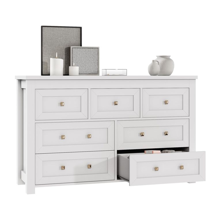 a white dresser with drawers next to a vase and candle holders on top of it