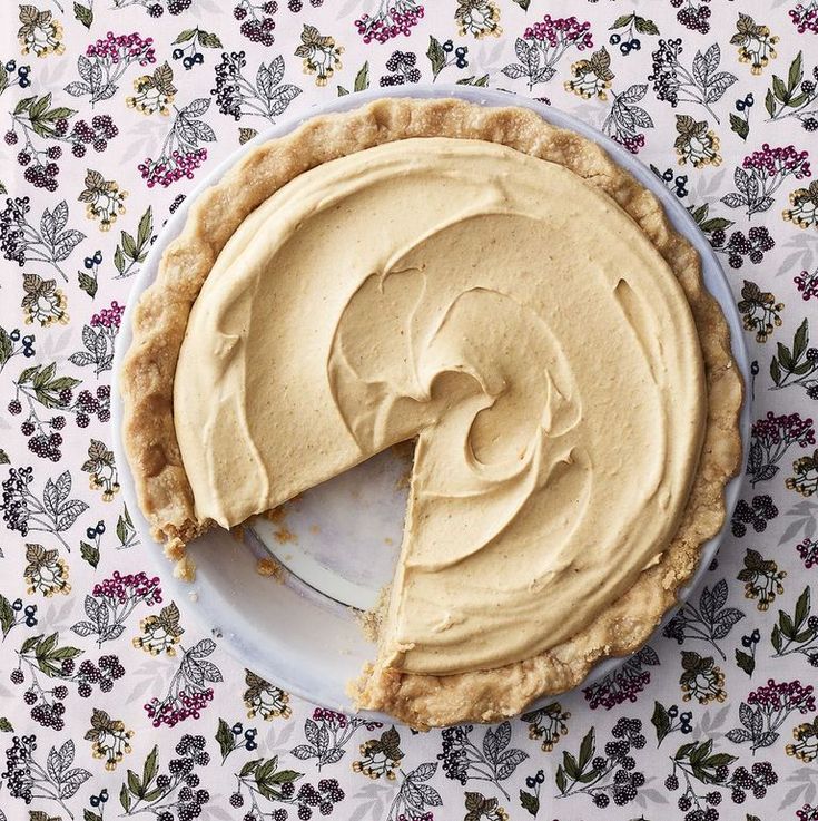 a pie with a slice missing from it on a tablecloth covered plate and flowers