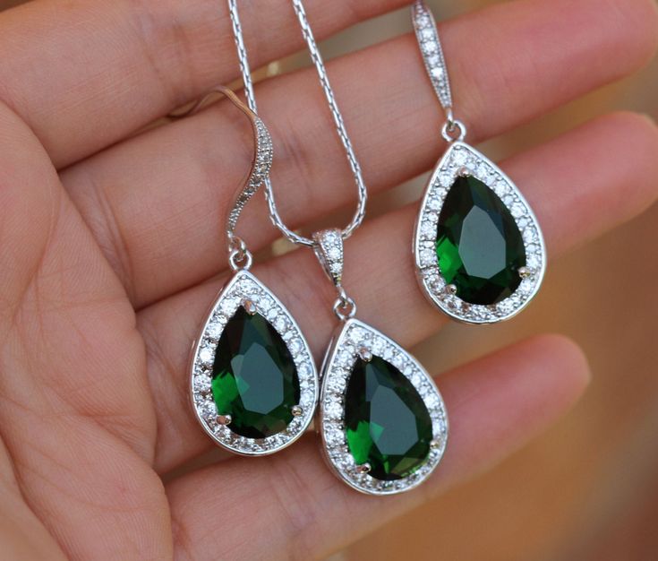 a person holding two green and white necklaces in their hand with diamonds around them