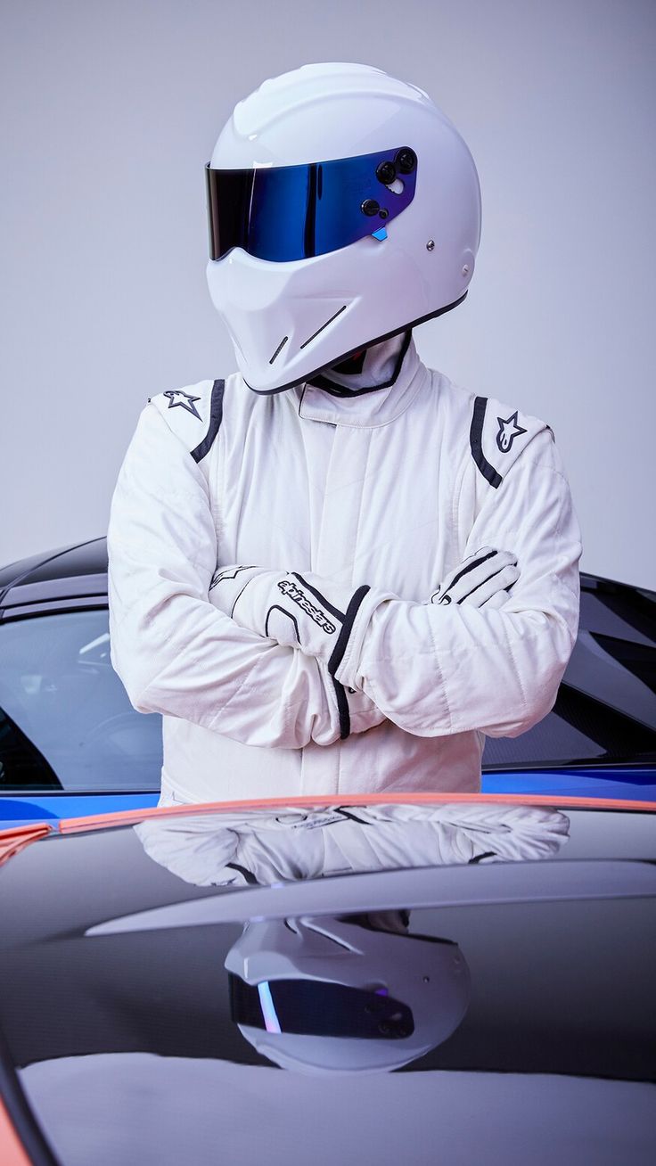 a man in a white suit and helmet leaning on the hood of a sports car