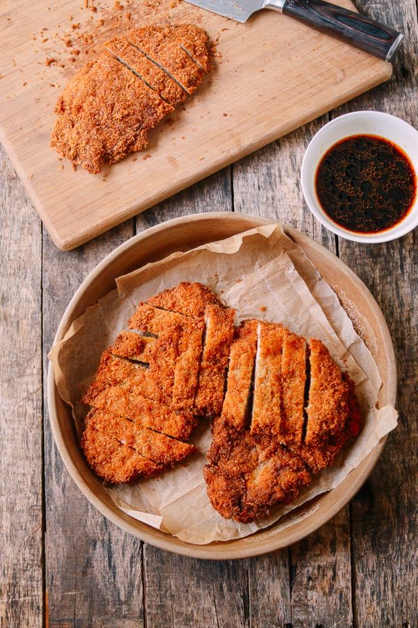 two pieces of fried chicken sitting on top of a wooden cutting board next to a bowl of sauce