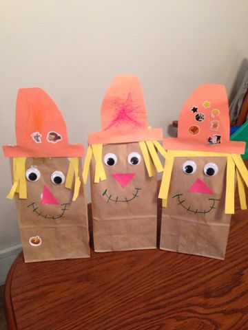 three paper bags with faces made to look like scarecrows sitting on top of a table