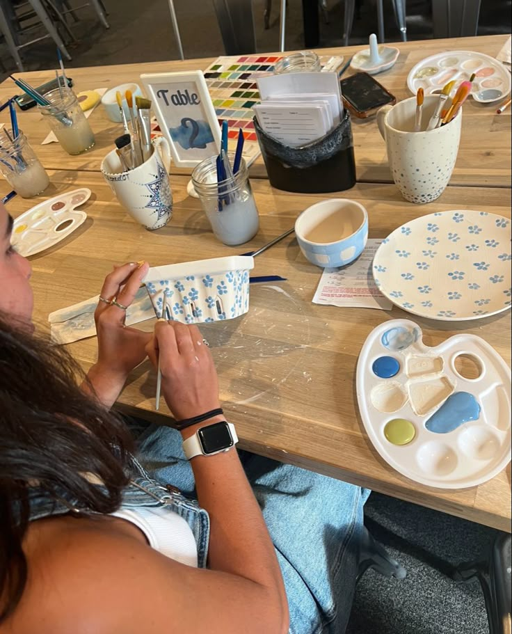 a woman sitting at a table working on some crafting supplies with scissors and paint