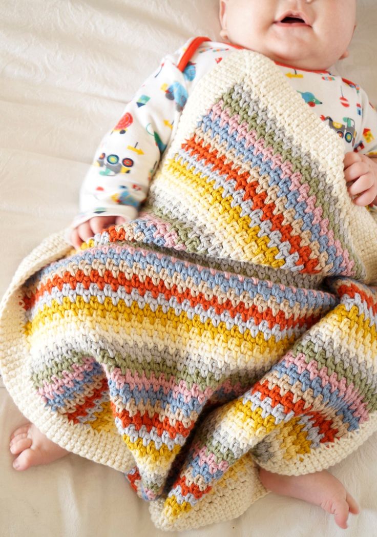 a baby laying on top of a bed covered in a colorful crochet blanket