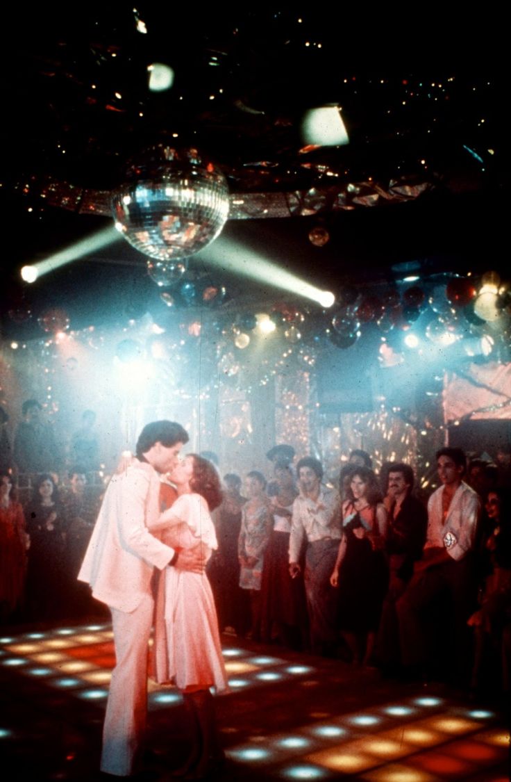 a couple kissing on the dance floor in front of an audience at a disco ball