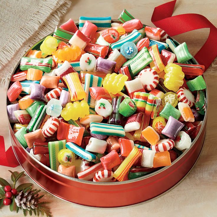 a tin filled with assorted candy on top of a wooden table next to a red ribbon