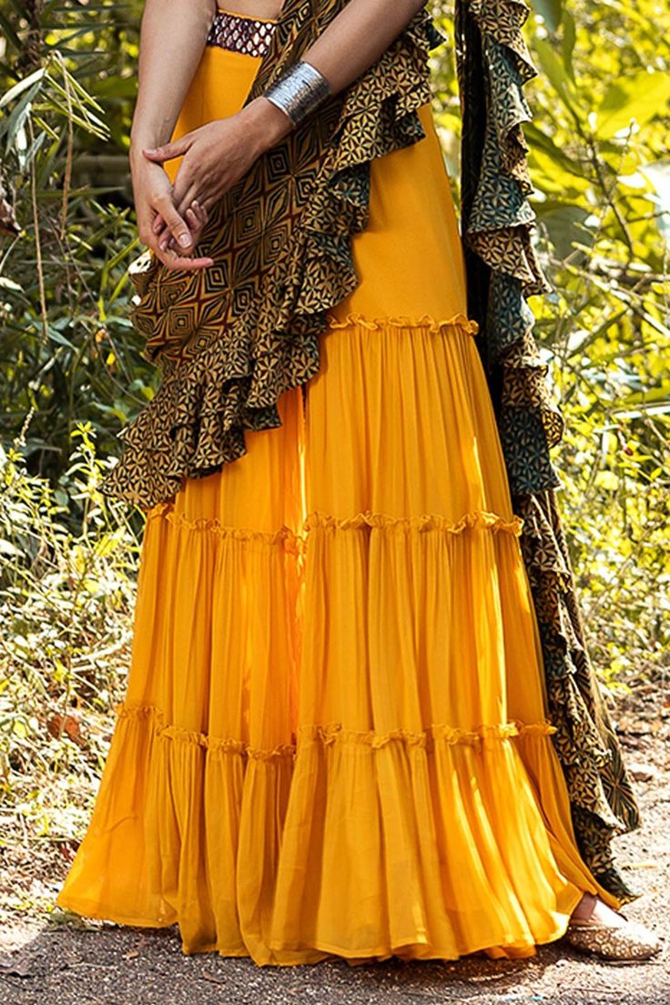 Mustard yellow tiered sharara paired with mirror embroidered blouse. Comes with printed ruffle dupatta.
Component: 3
Pattern: Embroidered, Printed
Type Of Work: Thread work Embroidery
Neckline: One shoulder
Sleeve Type: Sleeveless
Fabric: Georgette, Raw Silk, Silk
Color: Yellow
Other Details: 
Scalloped hem blouse
Ruffle dupatta
Tiered sharara
Occasion: Mehendi and Haldi - Aza Fashions Yellow Bohemian Saree Set, Bohemian Yellow Saree Set, Yellow Ruffled Wedding Sets, Traditional Yellow Ruffled Sharara, Yellow Bohemian Designer Sharara, Yellow Bohemian Lehenga For Festive Occasions, Diwali Anarkali Traditional Wear With Ruffles, Bohemian Yellow Lehenga For Diwali, Bohemian Yellow Lehenga For Festive Occasions