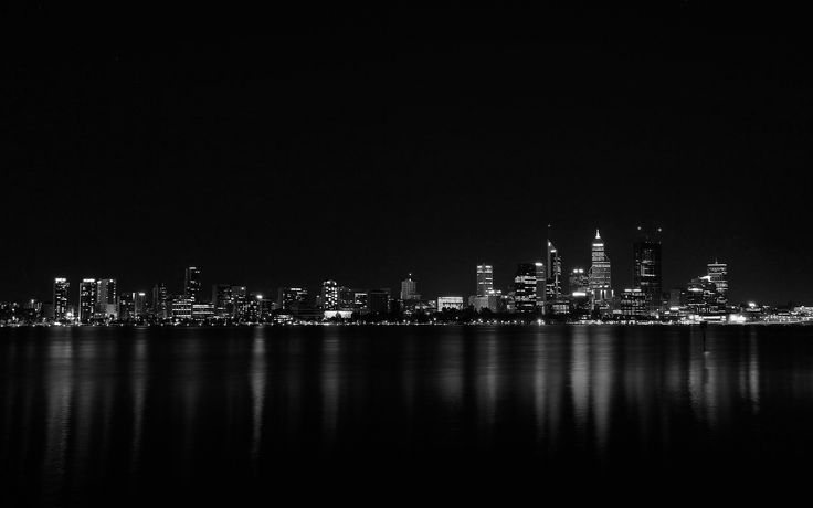 black and white photograph of the city skyline at night with water reflecting off it's surface