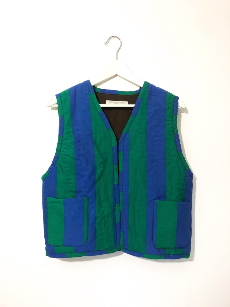 a blue and green striped vest hanging on a white wall with a black shirt underneath it