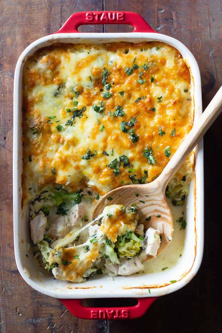 a casserole dish with chicken, broccoli and cheese in it next to a wooden spoon