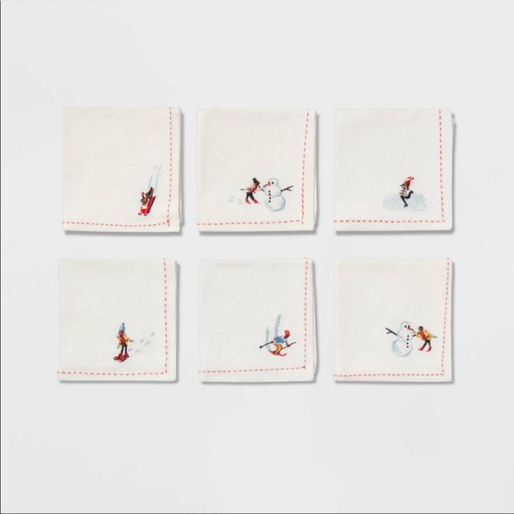 four white napkins with red stitching on them and snowmen in the background