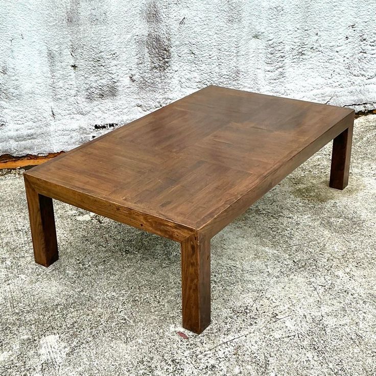 a wooden table sitting on top of a cement floor next to a white brick wall