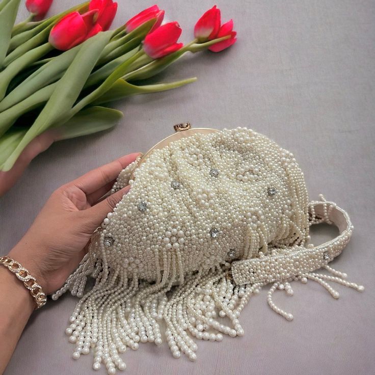 Step into a world of timeless elegance with our exquisite handmade ivory beaded bridal potli bag. Crafted with meticulous attention to detail, this enchanting accessory seamlessly blends tradition with modernity. Each delicate bead has been carefully chosen and skillfully hand-sewn, creating a mesmerizing symphony of shimmering ivory tones that catch the light with every movement. The potli bag's intricate beadwork showcases a stunning fusion of classic design and contemporary flair, making it a Traditional Evening Shoulder Bag With Pearl Handle, Evening Potli Bag With Pearl Handle, Wedding Embellished Pearl Evening Bag, Elegant Beaded Potli Bag For Party, Elegant Potli Bag With Pearl Embroidery For Party, Hand Embellished Rectangular Potli Bag For Weddings, Elegant Potli Bag With Pearl Embroidery For Reception, Elegant Pearl Embroidery Potli Bag For Formal Occasions, Traditional Evening Potli Bag With Pearl Handle