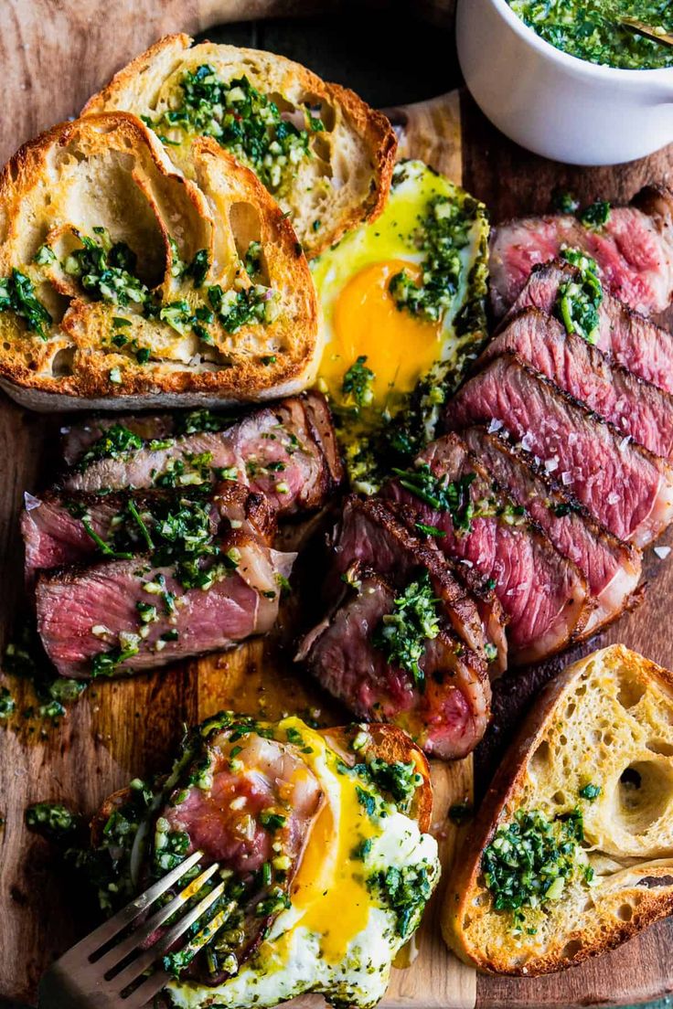 steak, eggs and bread on a cutting board with pesto sauce in a bowl