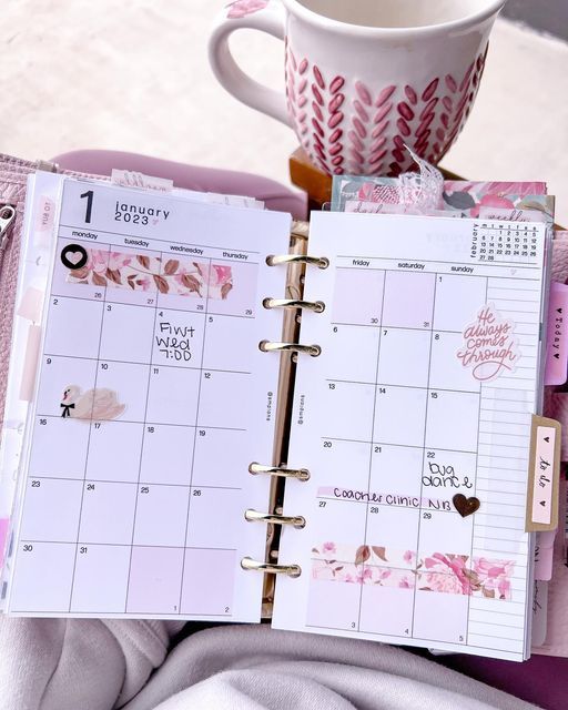 an open planner book sitting on top of a pink blanket next to a cup of coffee