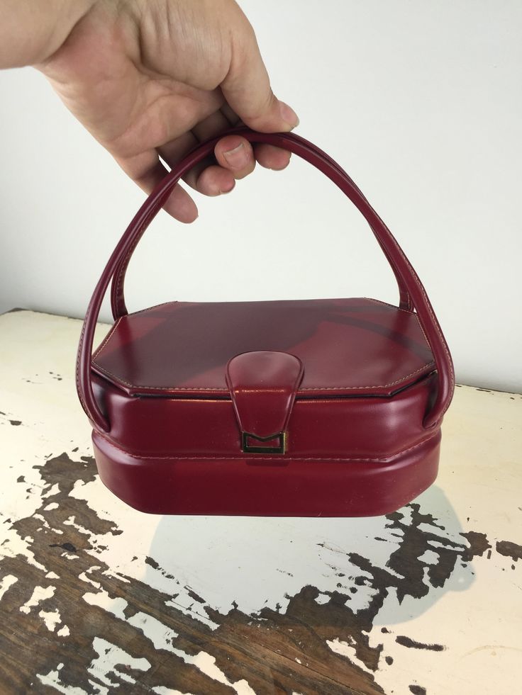 "Circa: 1950's Box bags coffin handbag oh so 1950s. Oxblood Burgundy vinyl faux leather octagon shaped coffin/box handbag with Two top handles. Long Octagon Coffin styled. She is strong and full of life left. Black rayon interior.  Very secure. DO YOU ACCEPT OFFERS? We do NOT accept offers or negotiate on pricing. We do offer layaways and have sales throughout the year. Shipping overages are always refunded. Label: Unmarked Fabric: brass tone metal, faux (vinyl) leather, rayon interior,  Conditi Retro Rectangular Box Bag For Evenings, Vintage Top Handle Box Bag For Formal Occasions, Vintage Box Bag For Formal Occasions, Vintage Leather Box Bag For Evenings, Retro Rectangular Evening Box Bag, Vintage Box Bag With Detachable Handle For Evening, Retro Satchel Box Bag, Red Leather Box Bag, Vintage Formal Top Handle Box Bag